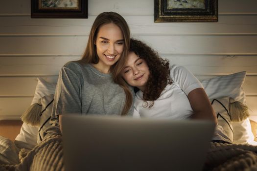 Two beautiful women lying in bed and watching movies on laptop at home