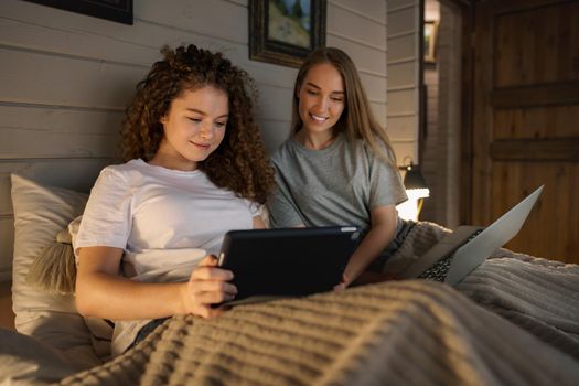 Two beautiful women lying in bed, holding and watching laptop