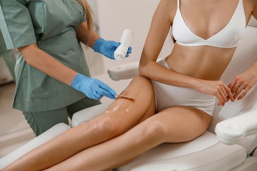 Special ointment applied on legs before laser epilation procedure in beauty salon. Hair removal