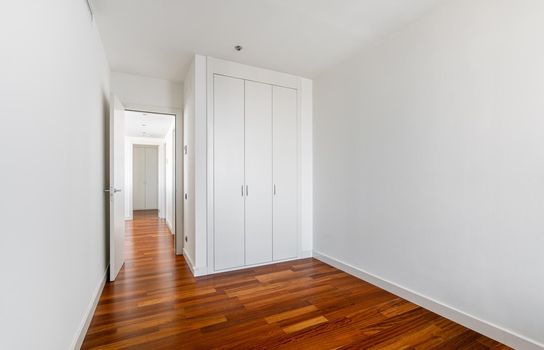 Interior of empty apartment, white room with built-in wardrobe, parquet floor and view to the hallway.