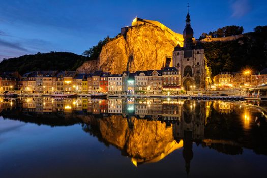 Night view of Dinant town, Collegiate Church of Notre Dame de Dinant over River Meuse and Pont Charles de Gaulle bridge and Dinant Citadel illuminated in the evening. Dinant, Belgium