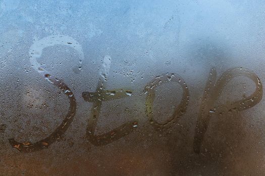 the word stop written on night wet window glass close-up with blurred background.