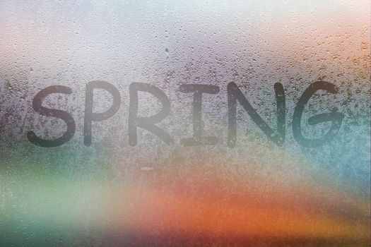 Foggy glass on window with written finger word spring on glass wet orange window in city on sunset.