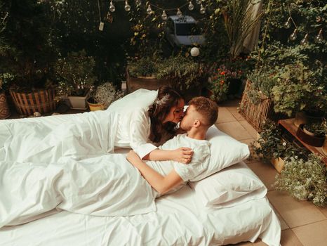 loving married couple lie on bed in hotel, relax together. man and woman in bathrobes have rest, leisure time, enjoy. look at each other with love