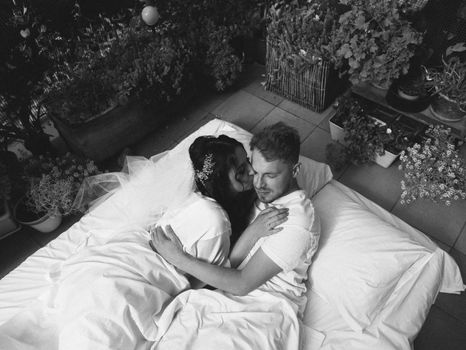 loving married couple lie on bed in hotel, relax together. man and woman in bathrobes have rest, leisure time, enjoy. look at each other with love