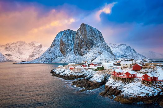 Famous tourist attraction Hamnoy fishing village on Lofoten Islands, Norway with red rorbu houses. With falling snow in winter on sunrise