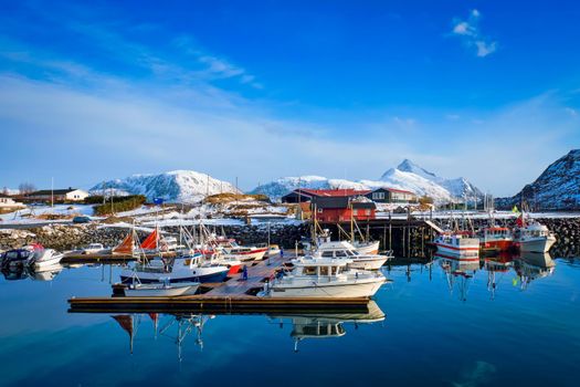 Fishing boats and yachts on pier in Norwegian fjord in village on Lofoten islands in winter, Norway