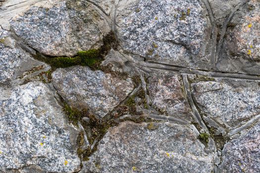 Aged and weathered white stone wall that has different size squares with mildew all over and deep crevices. Background texture