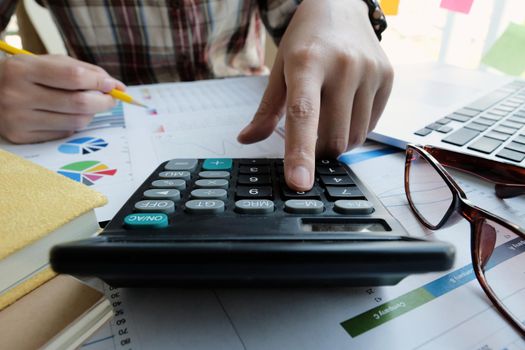 Close up Businesswoman using calculator and laptop for do math finance on wooden desk in office and business working background, tax, accounting, statistics and analytic research concept