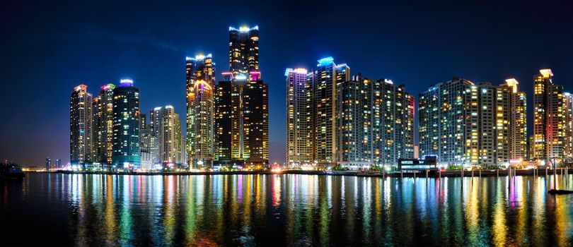 Panorama of Busan Marina city skyscrapers illluminated in night with reflection in water, South Korea