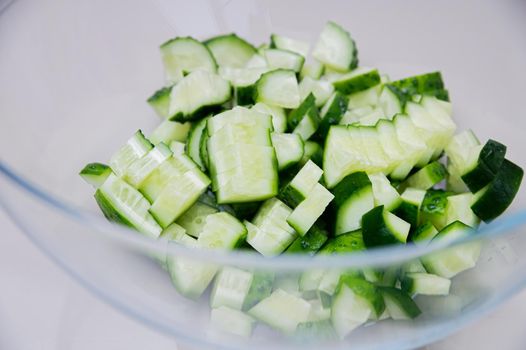 Fresh cucumber sliced for cooking vegetable salad in a glass transparent bowl on the kitchen table. Shallow depth of field.