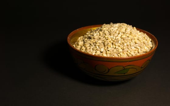 Scattered grains of oatmeal with a painted wooden cup on a black background.