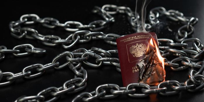 the Russian passport is on fire against the background of a metal chain
