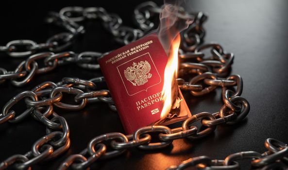 the Russian passport is on fire against the background of a metal chain