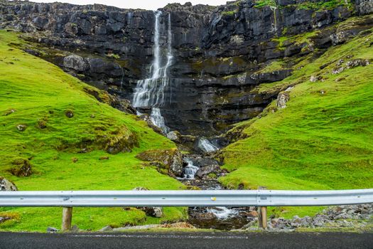 Waterfall over the rocks near the road with barrier