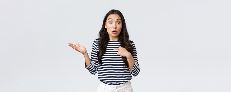 Lifestyle, beauty and fashion, people emotions concept. Shocked and surprised girl pointing at herself and shrugging as was picked or chosen, standing white background.