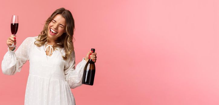 Holidays, spring and party concept. Portrait of excited and emotive good-looking blond girl dancing and celebrating, having fun saying yeah singing closed eyes, hold glass wine and bottle.