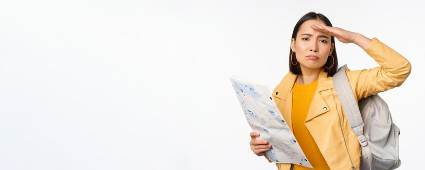 Image of young asian girl tourist, traveller with map and backpack posing against white studio background. Copy space