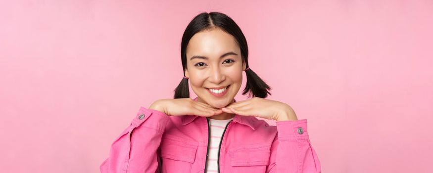 Skin care and cosmetology concept. Beautiful asian girl smiling and laughing, showing clean healthy facial skin, posing against pink background. Copy space