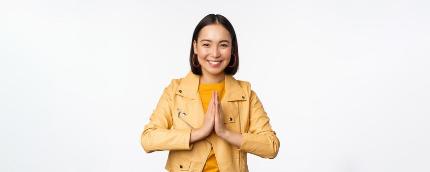 Happy korean woman, looking hopeful, asking for help favour, begging, standing with namaste gesture and smiling, standing over white background.