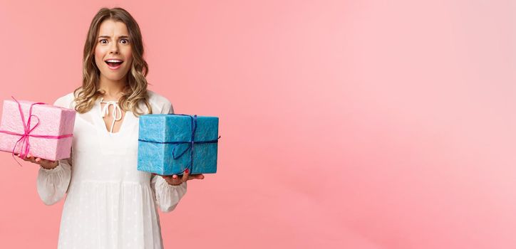 Holidays, celebration and women concept. Portrait of surprised and impressed blond girl didnt expect receive so many presents, holding two wrapped gifts and smiling camera astonished.