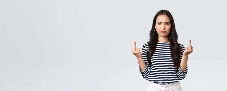 Lifestyle, beauty and fashion, people emotions concept. Pouting bothered young pissed-off asian female look annoyed and showing middle-fingers rude gesture, white background.