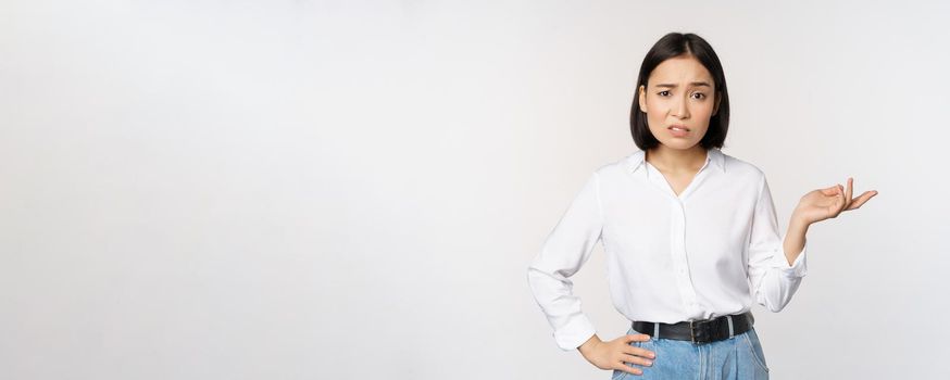 Portrait of confused asian woman asking so what, whats your problem gesture, staring puzzled, clueless and annoyed, standing over white background.