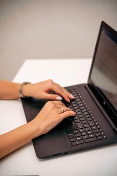 European professional woman sitting with laptop at home office desk, positive woman studying while working on PC. She is wearing a red plaid shirt and jeans