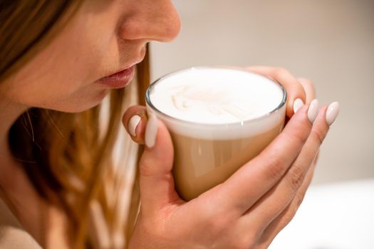 Close-up of beautiful female hands holding a large white cup of cappuccino. A woman is sitting in a cafe