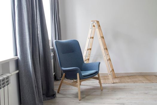 Room interior in Scandinavian style, in white and gray tones. A gray armchair with wooden legs by the window.