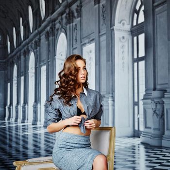 Beautiful girl in a striped shirt and tight skirt, black bra, curly hair, waist, hip, playful face, on a background of elegant background as a palace with columns, large windows and chic interiors. High quality photo