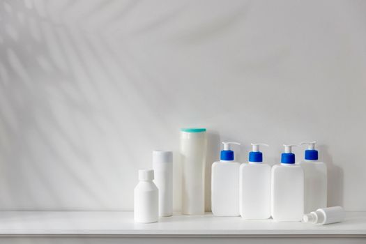White bottles with a blue dispenser with shampoo, conditioner, cream and liquid soap stand on a shelf in the bathroom. Place for text.