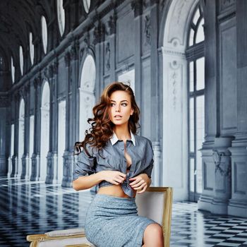 Beautiful girl in a striped shirt and tight skirt, black bra, curly hair, waist, hip, playful face, on a background of elegant background as a palace with columns, large windows and chic interiors. High quality photo
