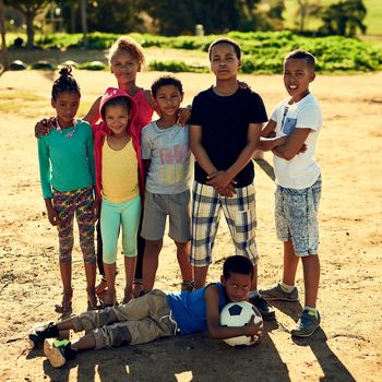 Portrait of a group of children standing together with a soccer ball outside.