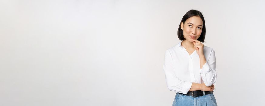 Image of thoughtful smiling woman has an idea, scheming, planning, looking aside and thinking, standing in office white blouse against studio background.