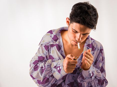 Young male in colorful clothes, looking down, lighting and smoking joint