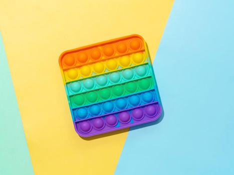 Popit on multicolor background with copy space. Popular silicone colorful antistress pop it toy for child on blue, yellow and blue paper background. Top view from above. Simple dimple