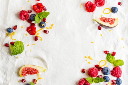 Whipped cream from egg whites with raspberries, blueberries, pomegranate, figs. Composition of berries with place for text on a white background. Layout. View from above.