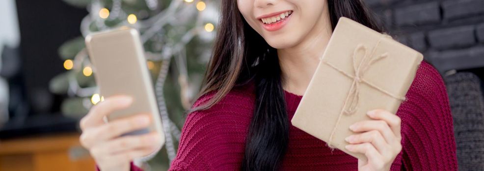 Young asian woman selfie video call online with friends and show gift box in Christmas day on phone at home, social distancing, new normal, female video conference, communication and holiday concept.