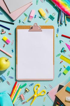 Clipboard with empty white sheet and school stationery. Back to school concept with copy space over blue background. Vertical. Trendy clipboard mockup. Flat lay, top view