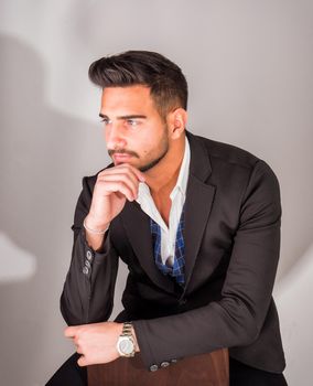 Young businessman wearing business suit, on light background, sitting