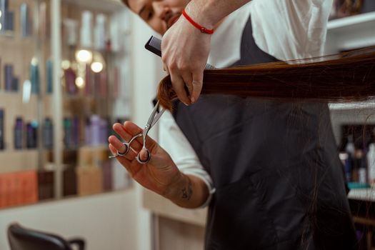 Closeup of hairdresser hands holding a comb while cutting hair of woman. Hair care, beauty