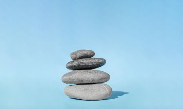 Balanced pebble stones for spa treatments on blue background. The balancing cairn - symbol of harmony, tranquility and relaxation, concept of meditation. Stack of spa hot stones.