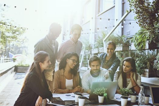 Shot of a team of colleagues using a laptop together during a meeting at an outdoor cafe.