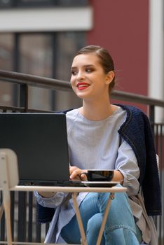 Charming happy woman student using laptop computer to prepare for the course work. Concept of working outdoors