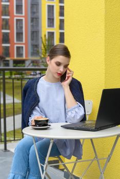 Charming happy woman student communicates by phone and use laptop computer to prepare for the course work. Concept of working outdoors