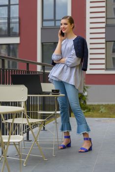 Charming happy woman student communicates by phone and use laptop computer to prepare for the course work. Concept of working outdoors