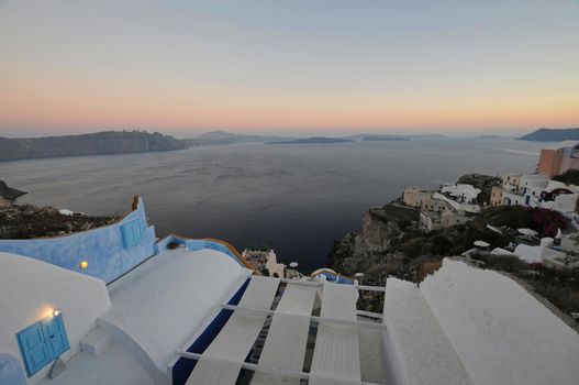 Scenic view of traditional cycladic Santorini houses on small street with flowers in foreground. Location: Oia village, Santorini, Greece. Sunset view point. Holidays background.