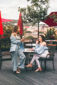 two young women friends at a cafe having breakfast, discussing the news, laughing. females in the cafe drink cocktails. two attractive young women relaxing