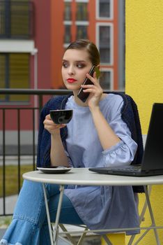Charming happy woman student communicates by phone and use laptop computer to prepare for the course work. Concept of working outdoors